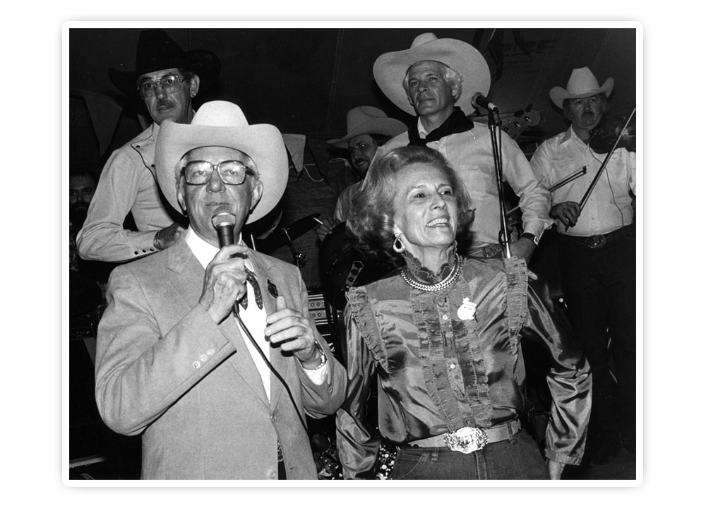 This is a black-and-white photo of Mr. John S. Justin, Jr. and Mrs. Jane Chilton Justin posing for a photo while Mr. Justin is speaking in a microphone.